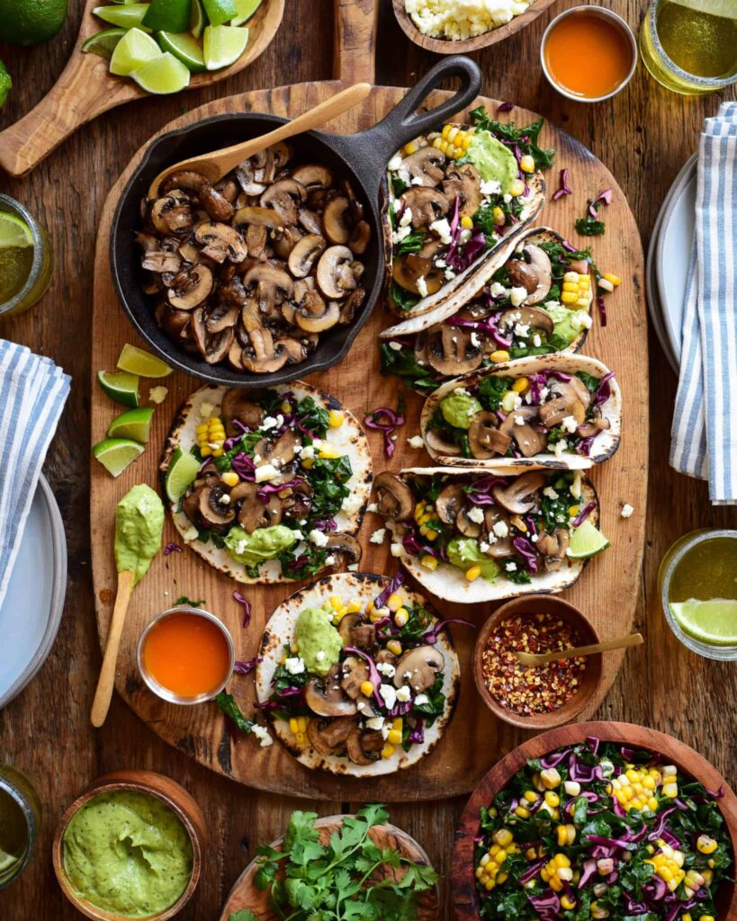A mushroom taco board with six loaded tacos surrounded with extra toppings.
