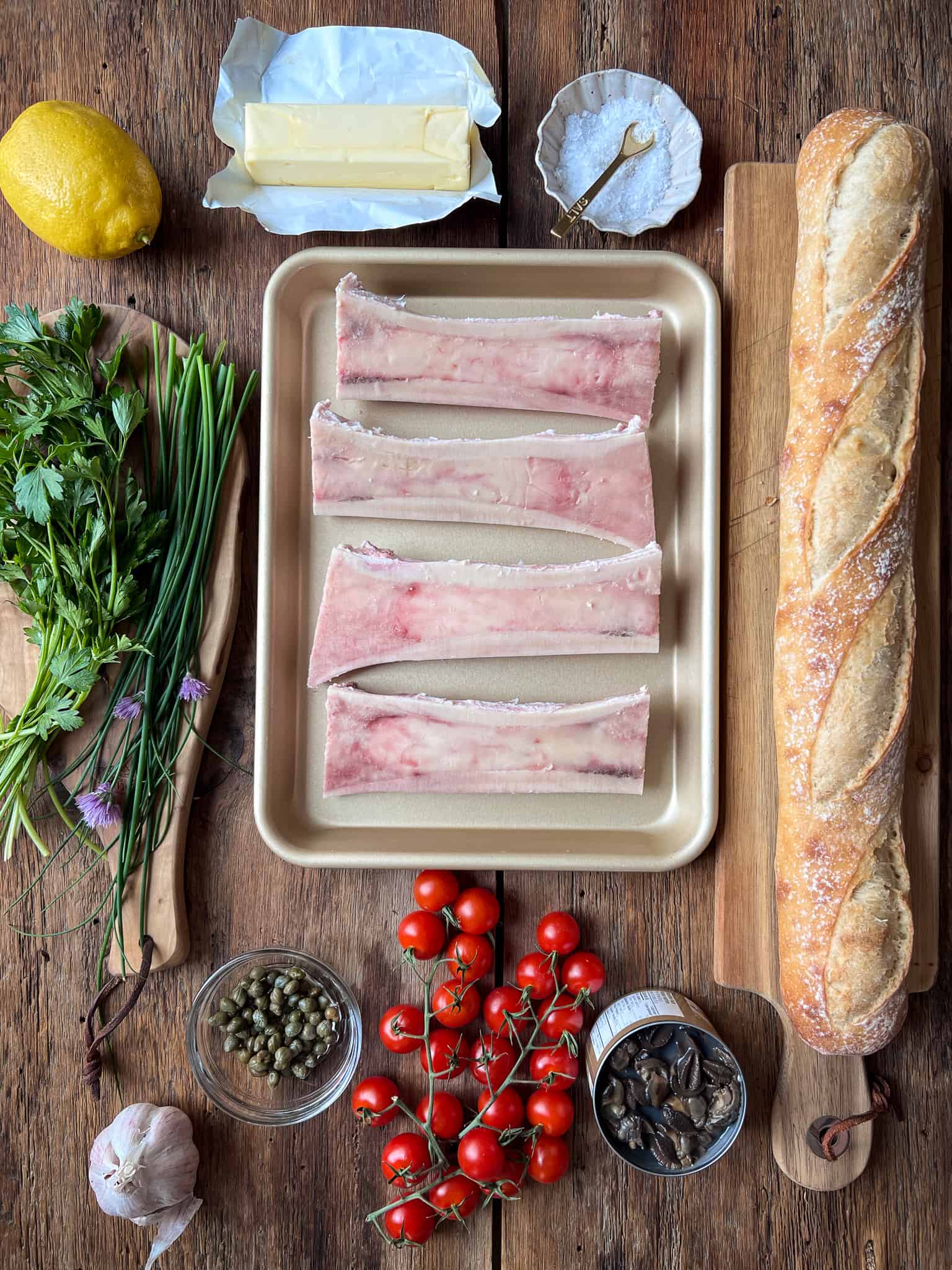 Four canoe bone marrow bones plus ingredients to make Sous-Vide Bone Marrow with Garlic Butter Escargot, Tomatoes and Chive Flowers.