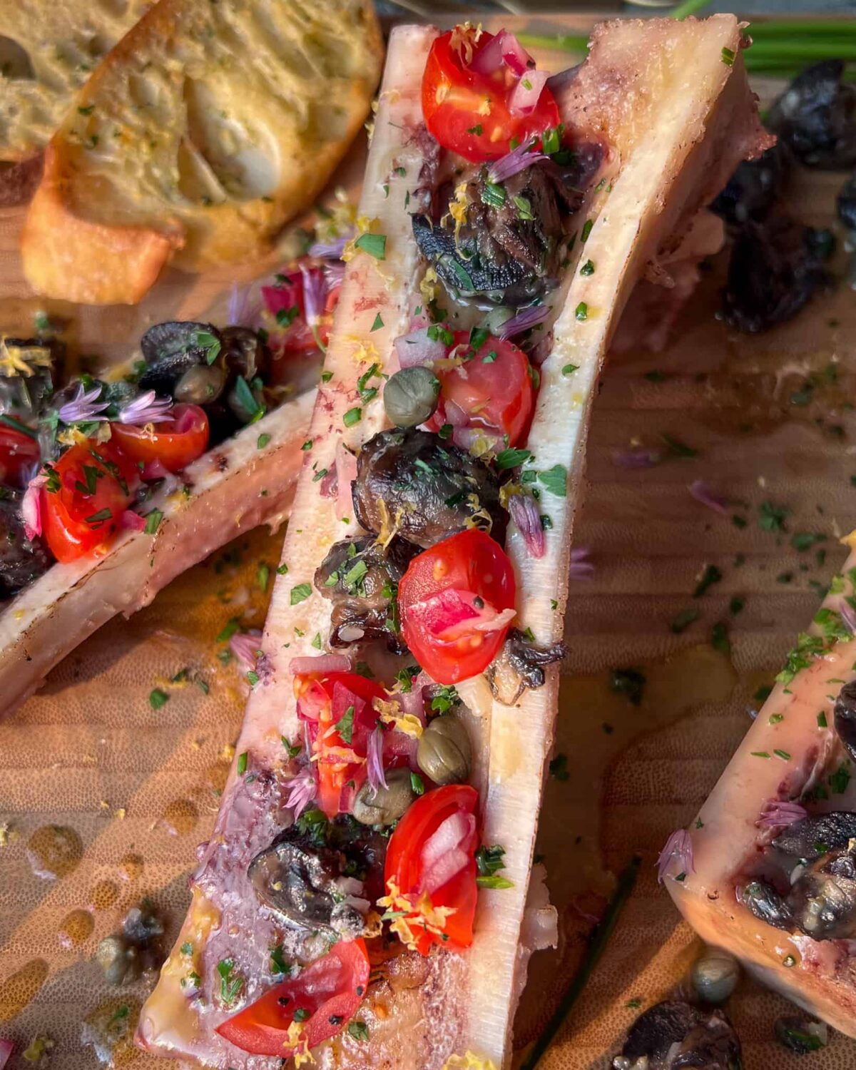 A close up of a canoe cut bone marrow with escargots and tomatoes.