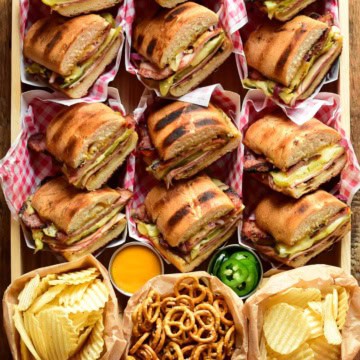 A tray of grilled Cuban sandwiches (Cubano) with chips and pretzels.