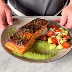 Pan Seared Blackened Salmon served with a schmear of crema on the plate, a serving of rice and a simple village salad.