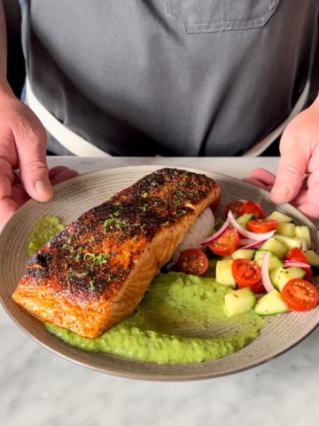 Pan Seared Blackened Salmon served with a schmear of crema on the plate, a serving of rice and a simple village salad.