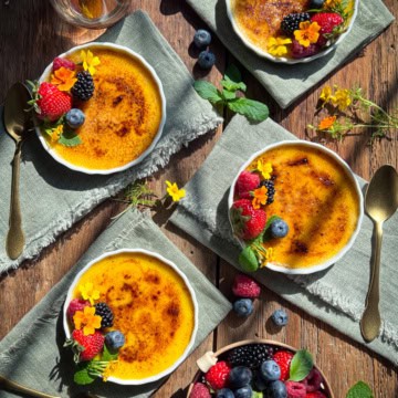 Four crème brûlée on napkins topped with berries and edible flowers.