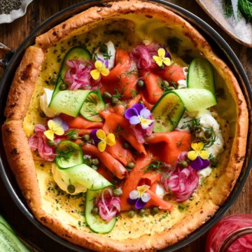 A Savory Dutch Baby with Smoked salmon cream cheese, capers, pickled onions, cucumber, fresh herbs, everything bagel seasoning and edible flowers.