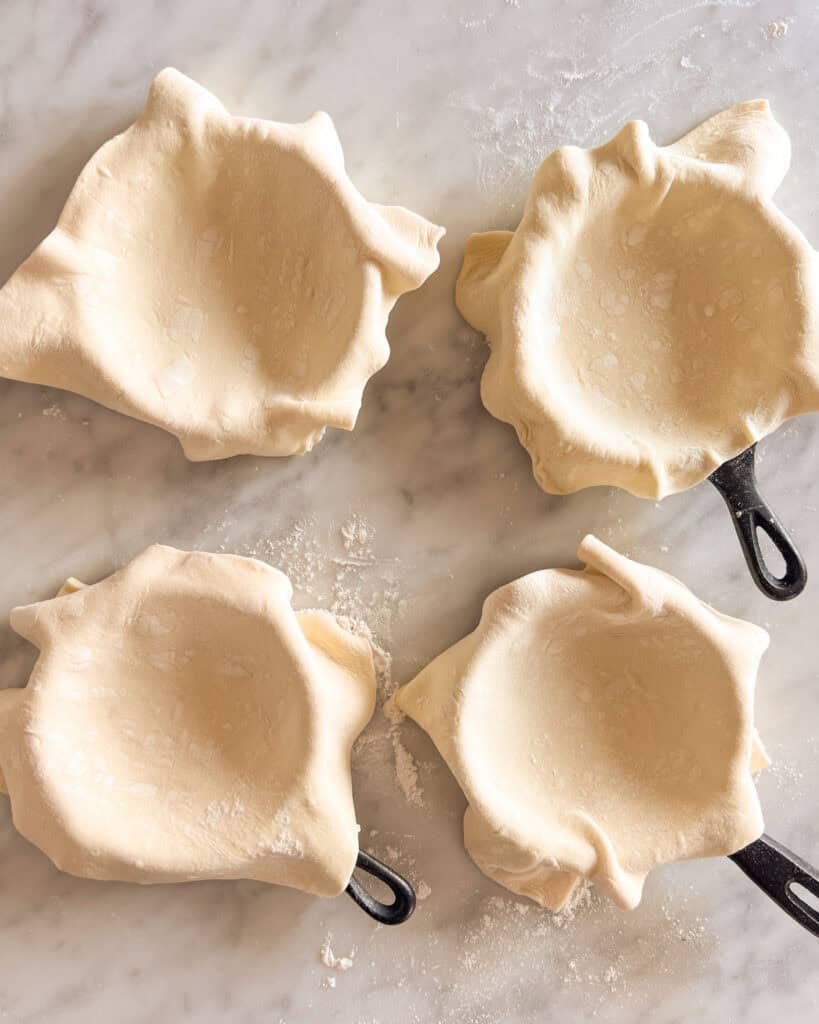 Four mini cast iron skillets draped with puff pastry.