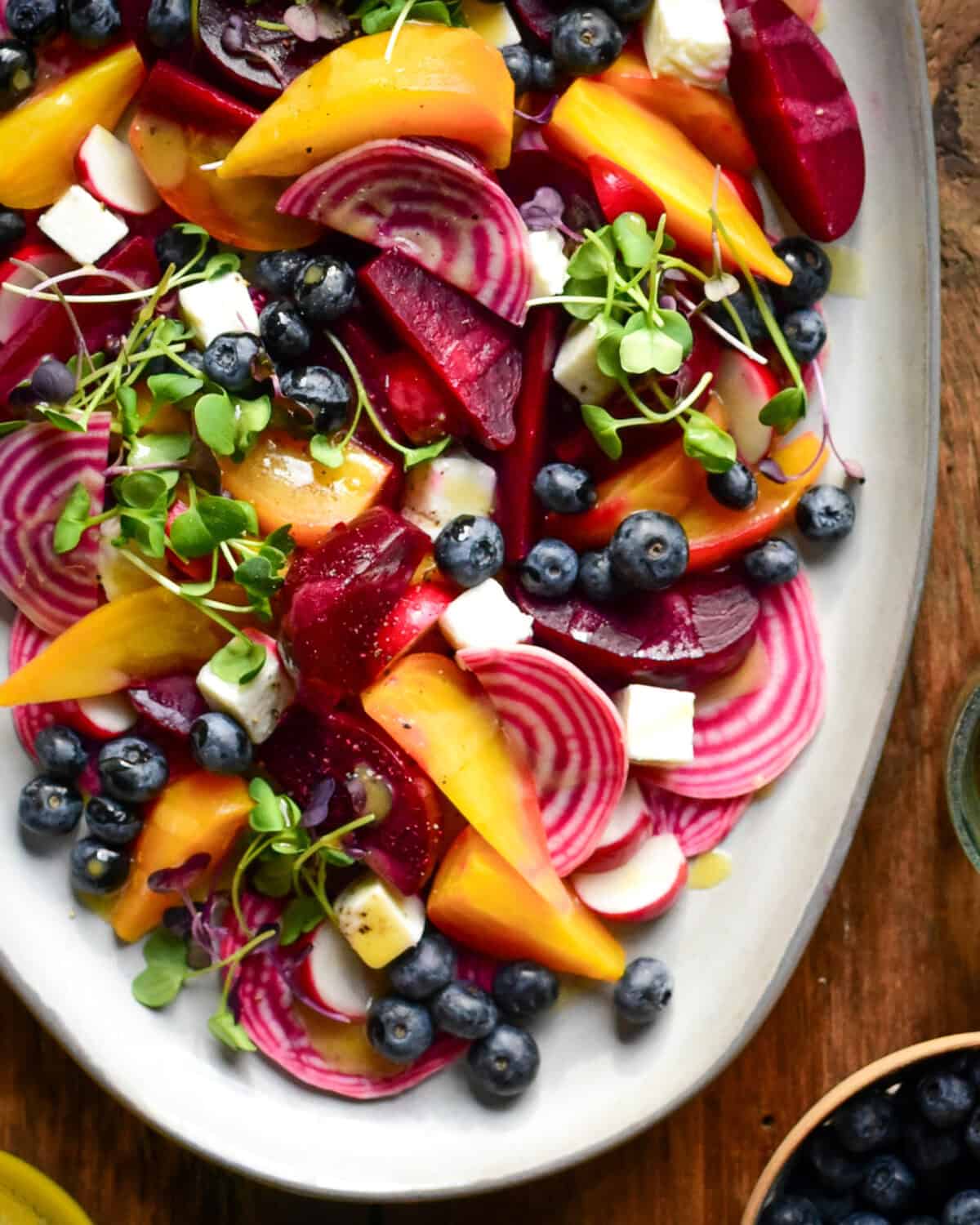 A close up of a sous-vide beet salad with three varieties of beets, radishes, blueberries, micro greens and feta cheese.