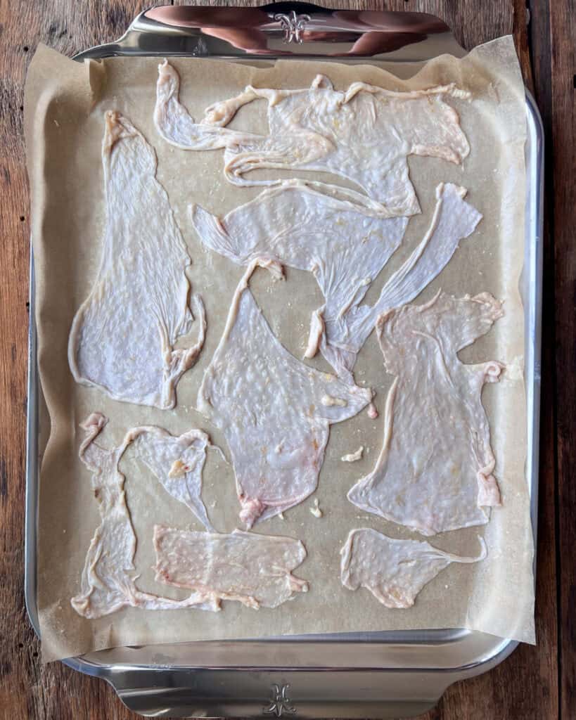 Chicken skins on a parchment lined sheet pan fat side down. Seasoned lightly with salt & pepper.