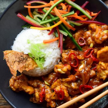 A close up of a bowl of Chili Chicken with Coconut Ginger Rice served with a carrot and cucumber salad and crispy chicken skins.