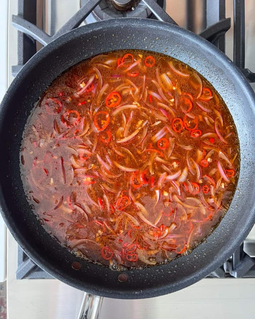 A simmering skillet of chili sauce with red chilis and onions.