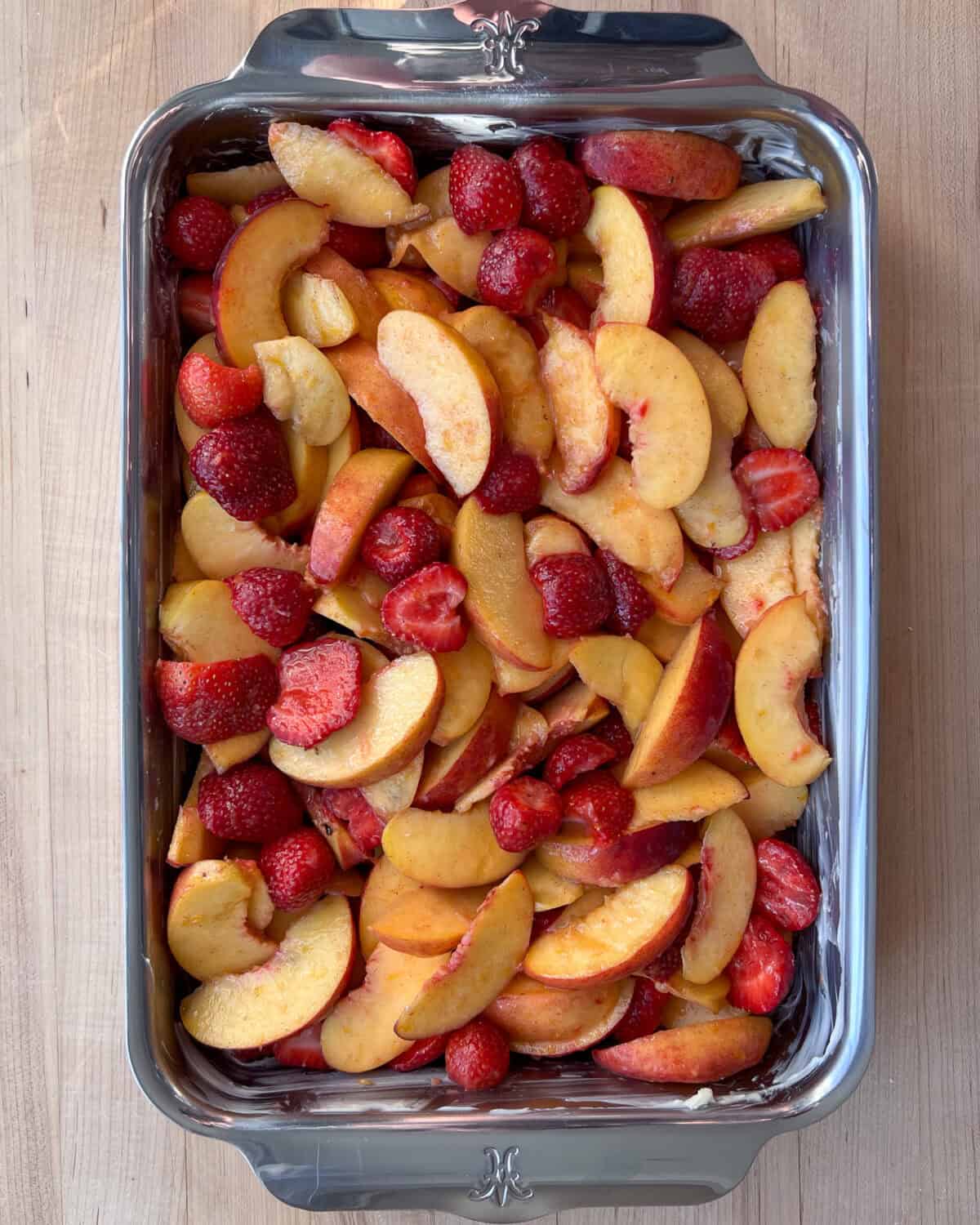 Sliced peaches and strawberries in a baking dish.