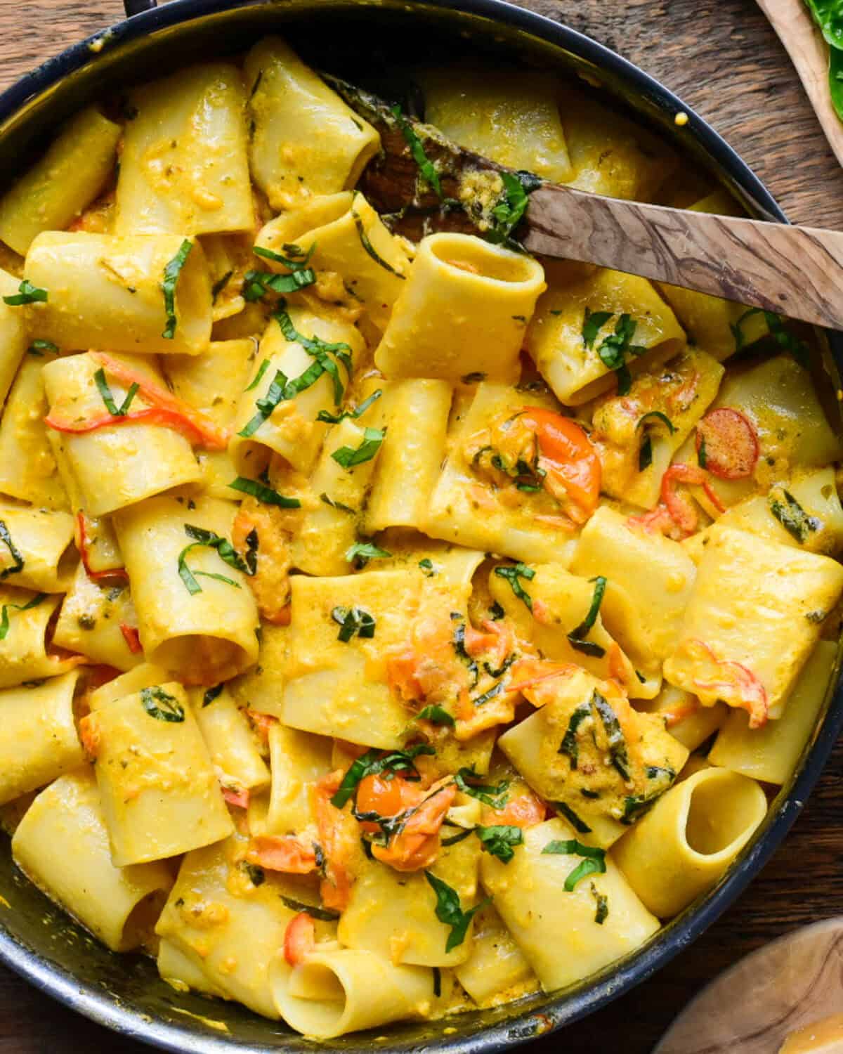 A pot of large tube pasta with a blistered orange grape tomato sauce.