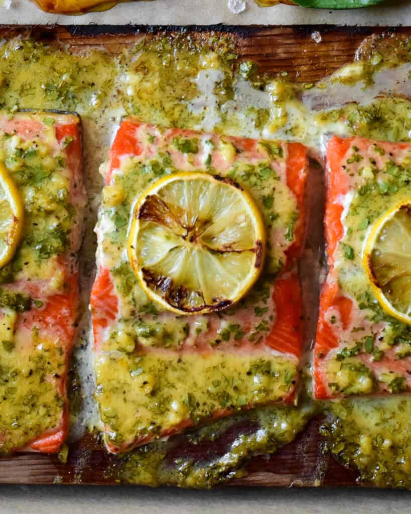 A close up of a piece of salmon with sauce and a grilled lemon on a cedar plank.