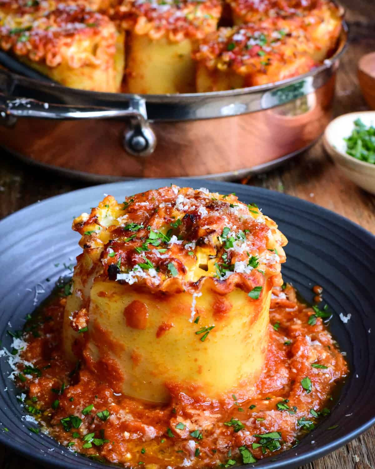 A copper pot of Butternut Squash Lasagna Roll Ups with a lasagna roll on a plate with Parma and chopped parsley.
