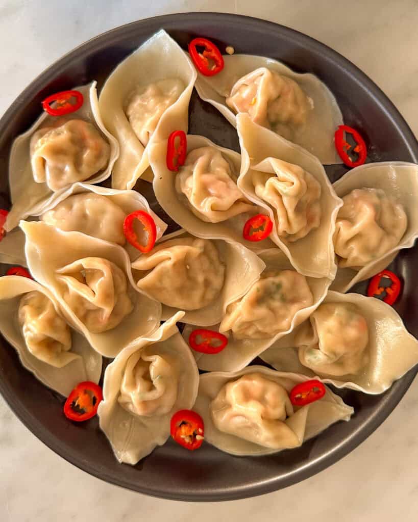 A plate of wontons with red chilies.