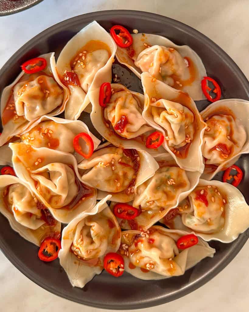 A plate of shrimp wontons with sauce and chilies.