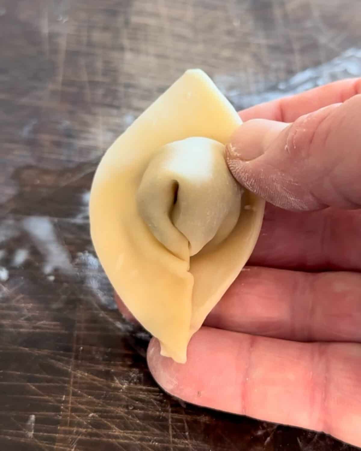 Dampen one of the base triangular tips with water. Bring the two base tips together, overlapping one over the other to create a boat shape. Press to seal, ensuring the wonton is closed.