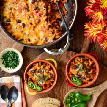 Two bowls and a large pot with a cheesy (Turkey) Chili Mac and Cheese. Served with jalapeno slices, chopped cilantro and bread.