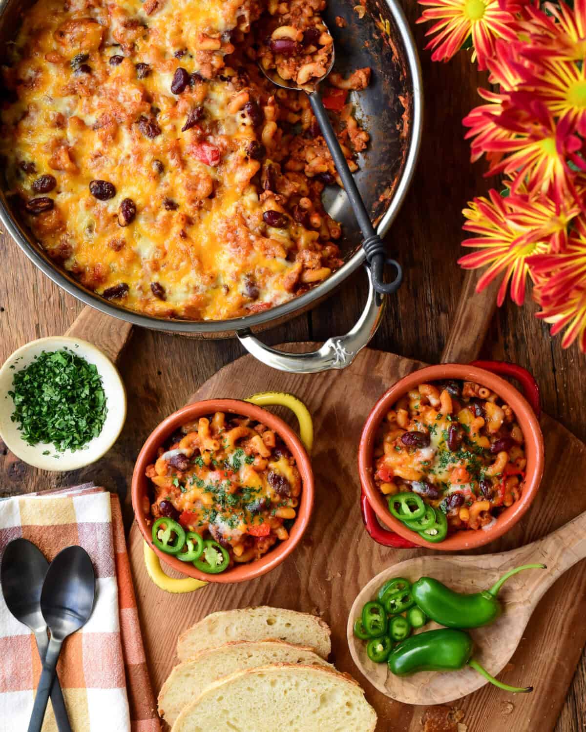 Two bowls and a large pot with a cheesy (Turkey) Chili Mac and Cheese. Served with jalapeno slices, chopped cilantro and bread.