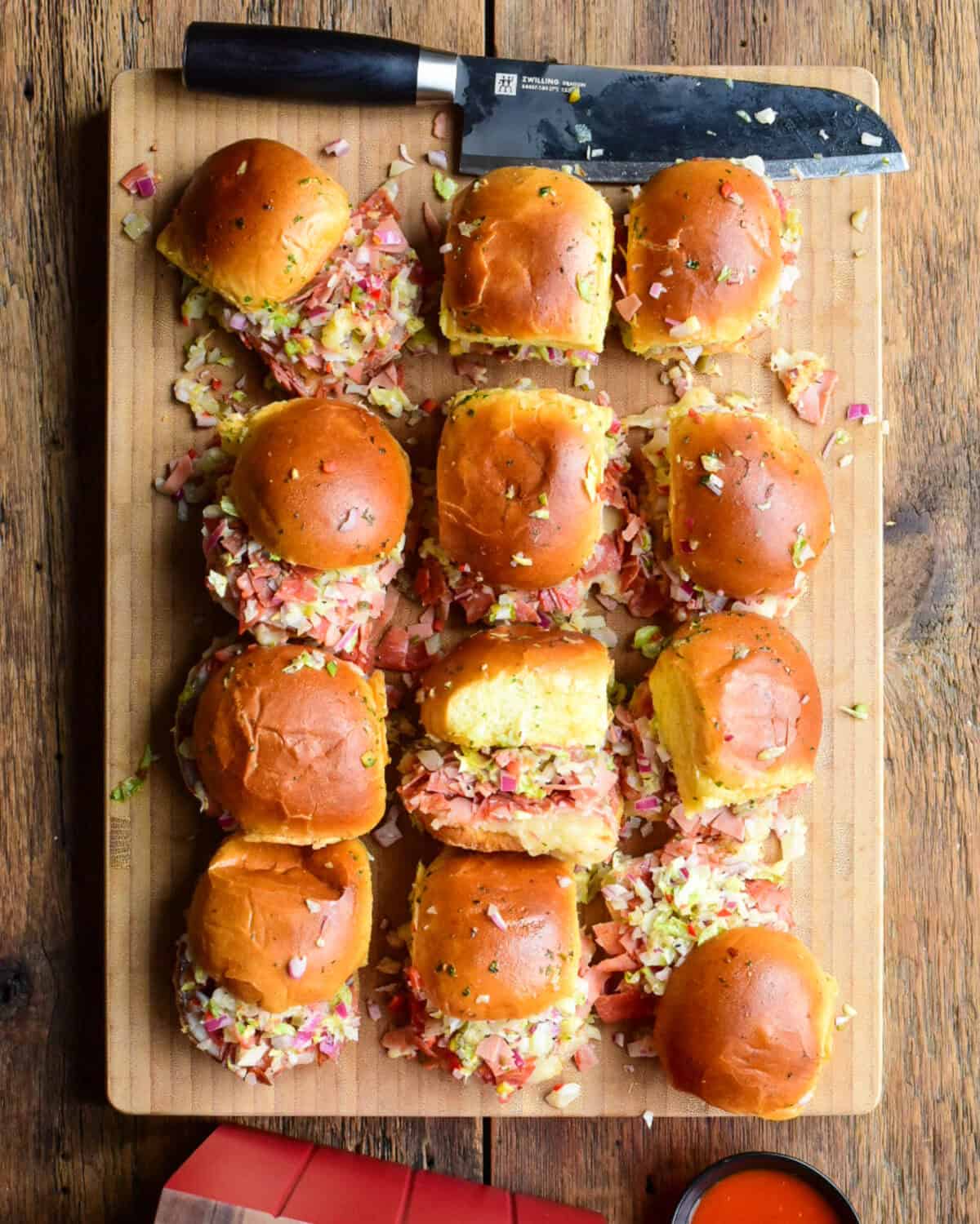 A wooden cutting board with twelve Chopped Italian Sliders.