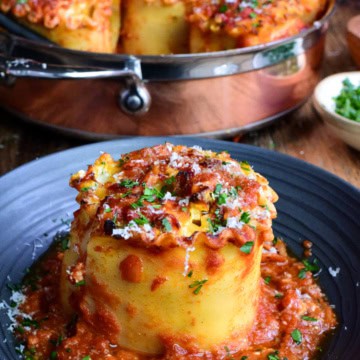 A copper pot of Butternut Squash Lasagna Roll Ups with a lasagna roll on a plate with Parma and chopped parsley.