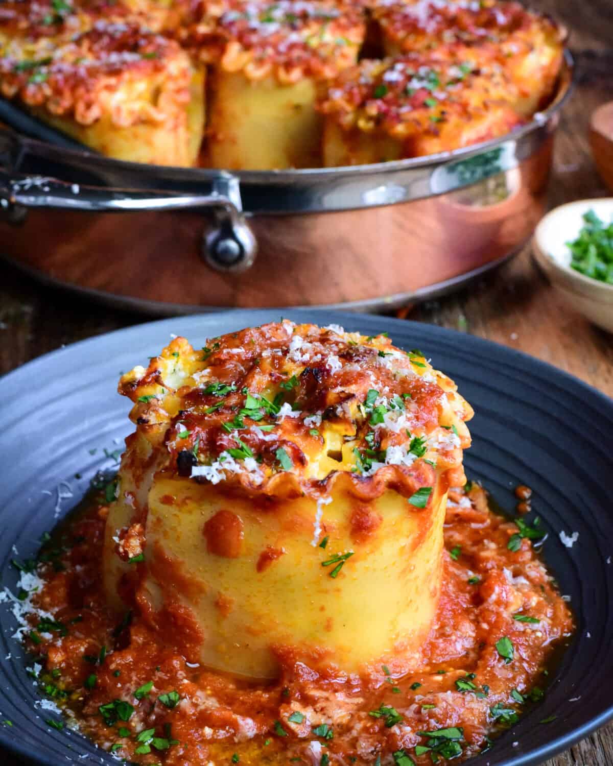 A copper pot of Butternut Squash Lasagna Roll Ups with a lasagna roll on a plate with Parma and chopped parsley.