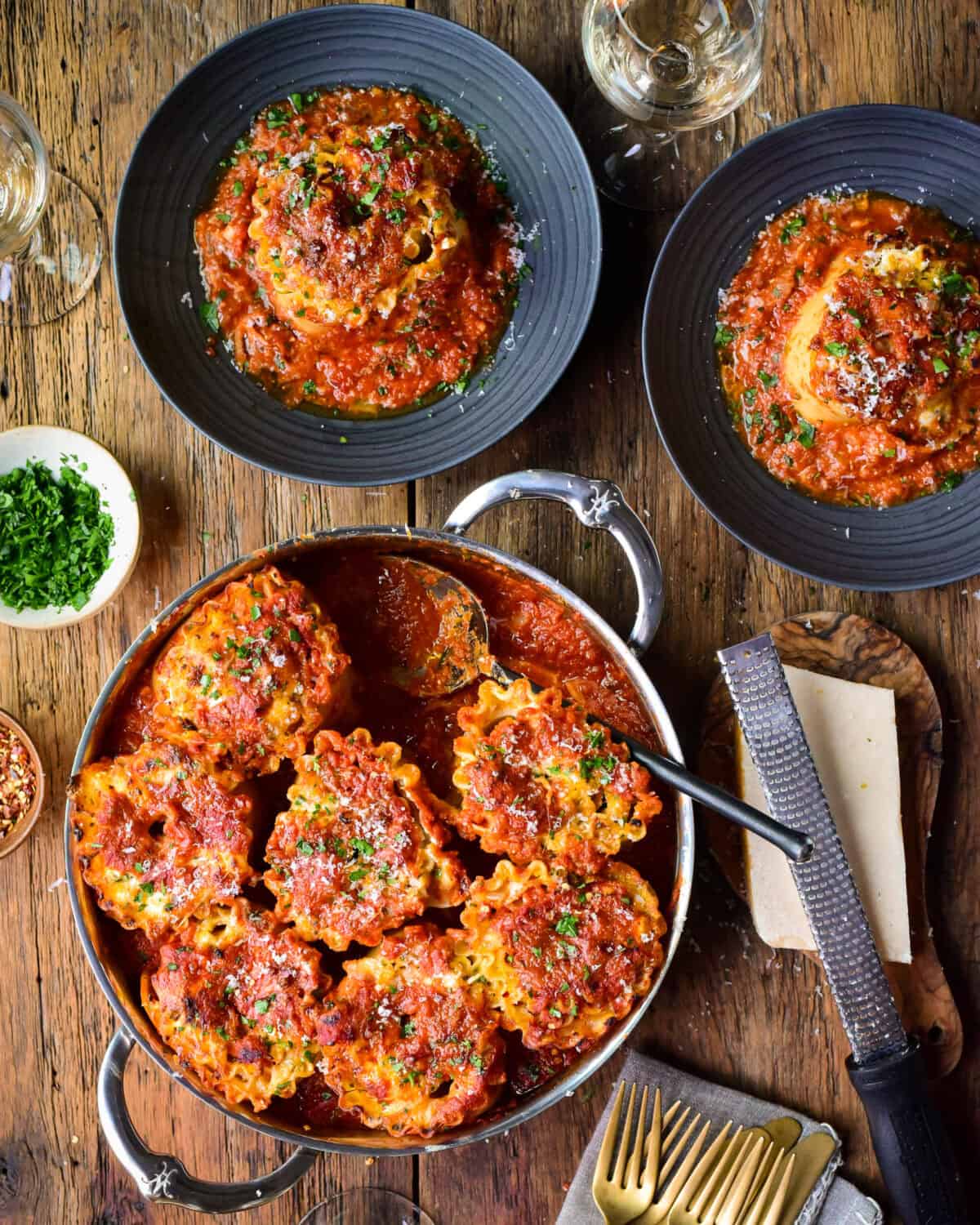A pan of rolled lasagna with two servings in a bowl and served with grated Parma and chopped parsley.