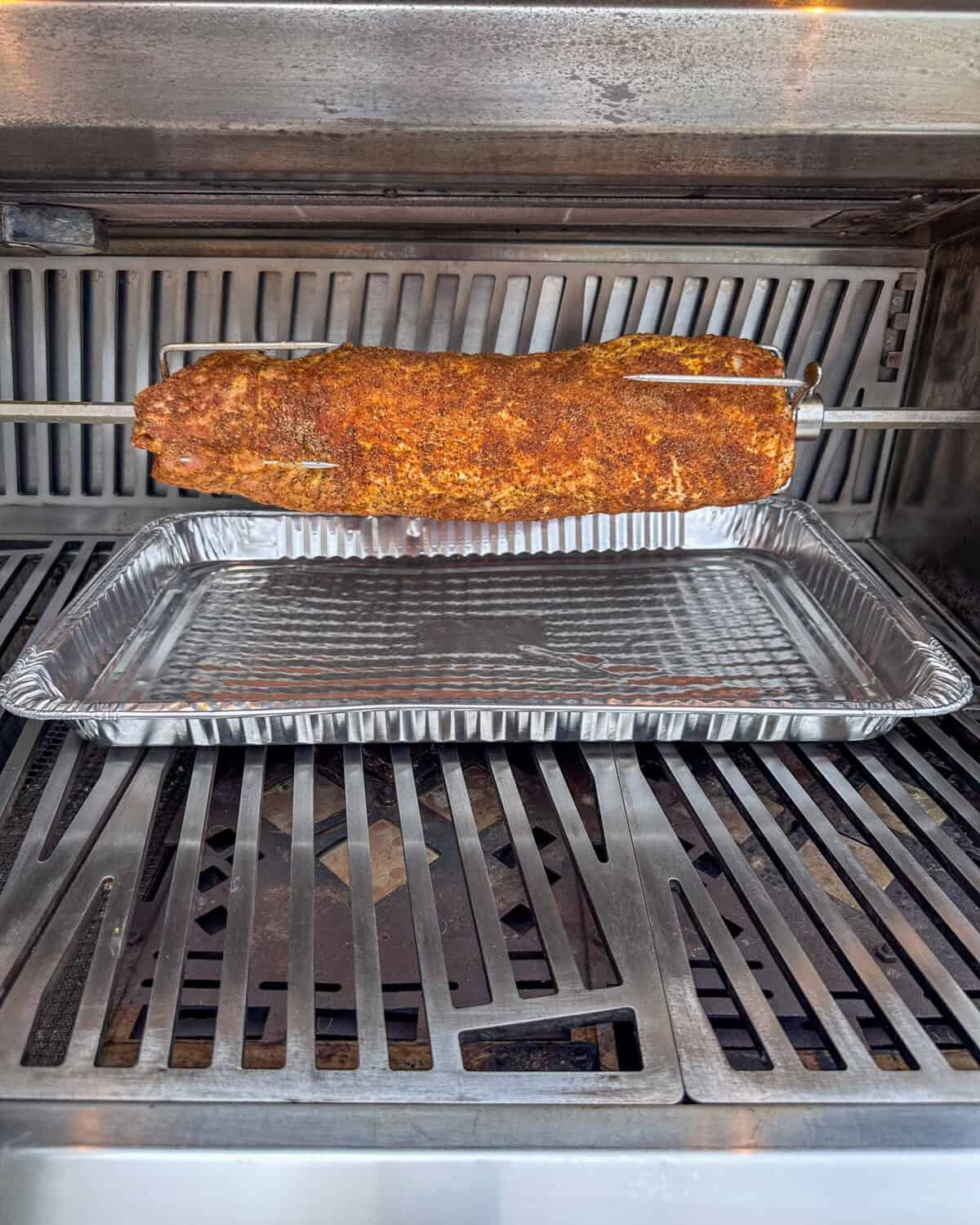 A pork loin on the rotisserie with a drip pan underneath it.