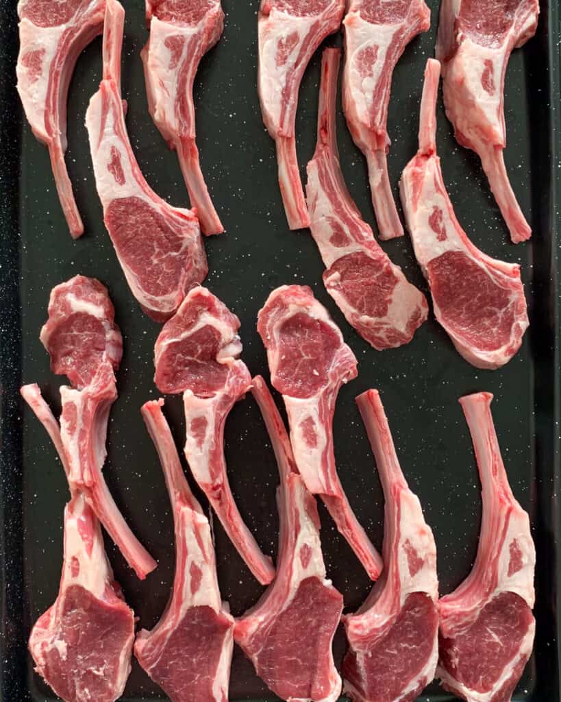 Two racks of lamb cut into individual chops on a sheet pan.