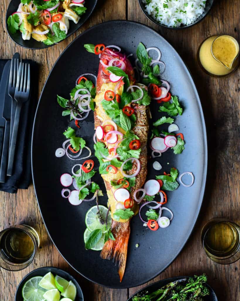 A grilled fish served with an herb salad and yellow curry sauce.