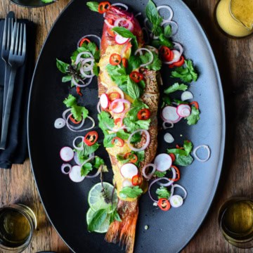 A whole red snapper served with yellow curry and a simple salad on a black serving platter.