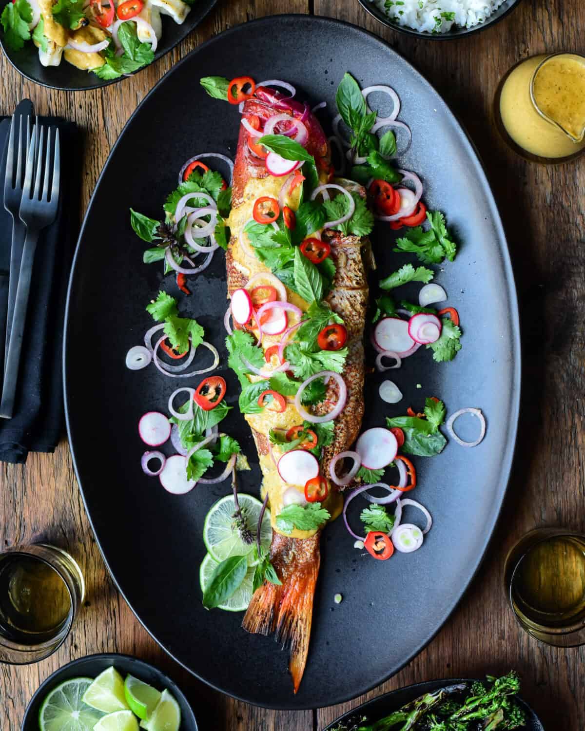 A whole red snapper served with yellow curry and a simple salad on a black serving platter.