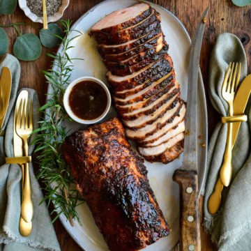 A platter of sliced Rotisserie Honey Garlic Pork Roast with a bowl of Marsala mushroom sauce.