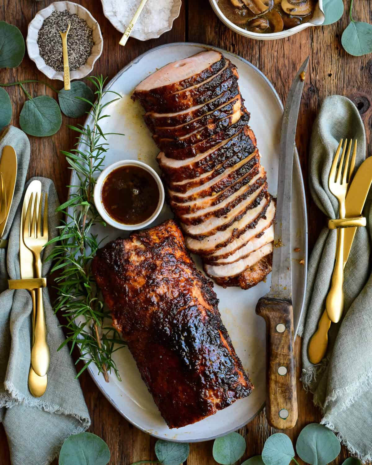 A platter of sliced Rotisserie Honey Garlic Pork Roast with a bowl of Marsala mushroom sauce.