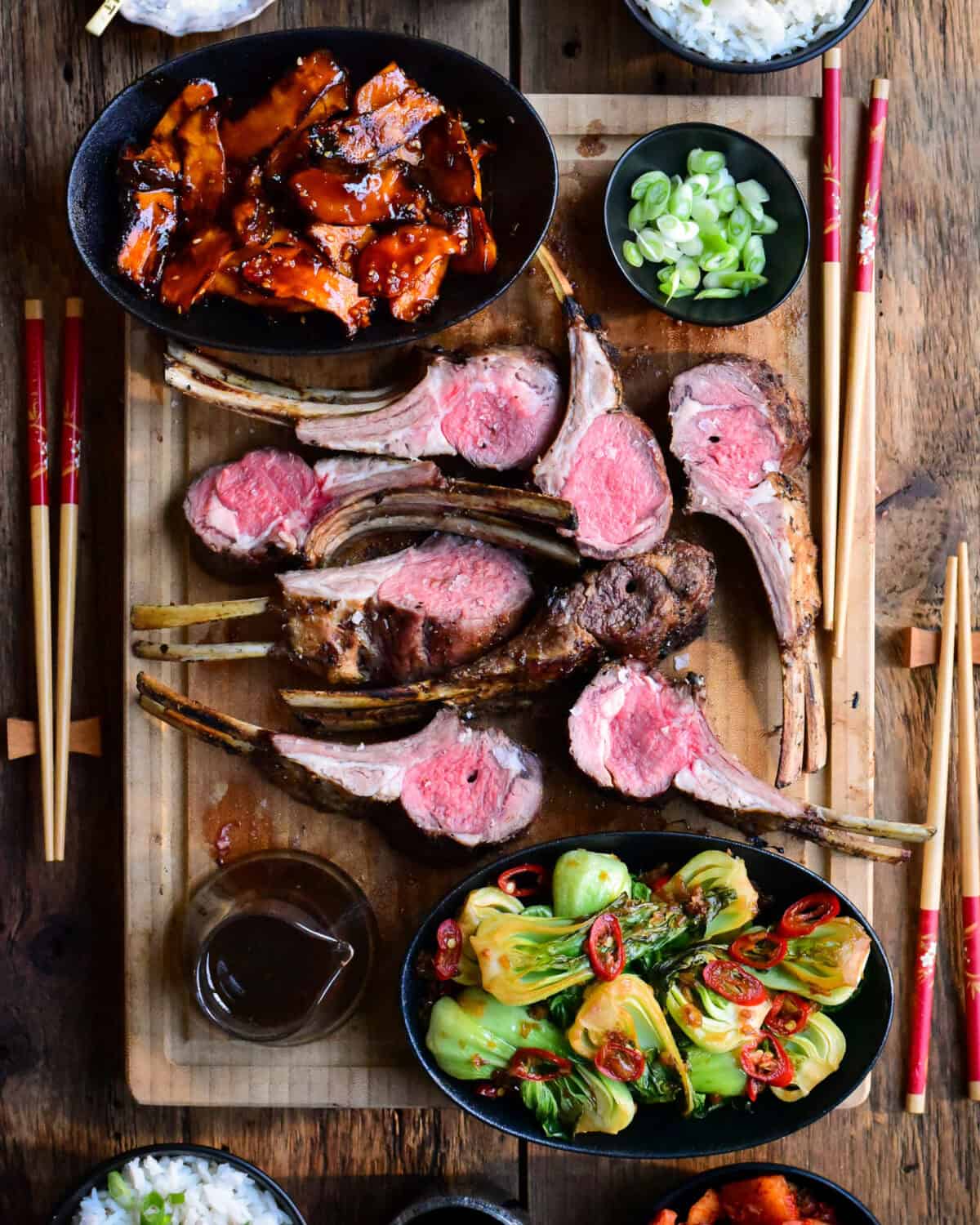 A serving board with two Grilled Frenched Rack of Lamb, cut open and served with Grilled Gochujang Mushrooms and Garlic-Ginger Bok Choy.