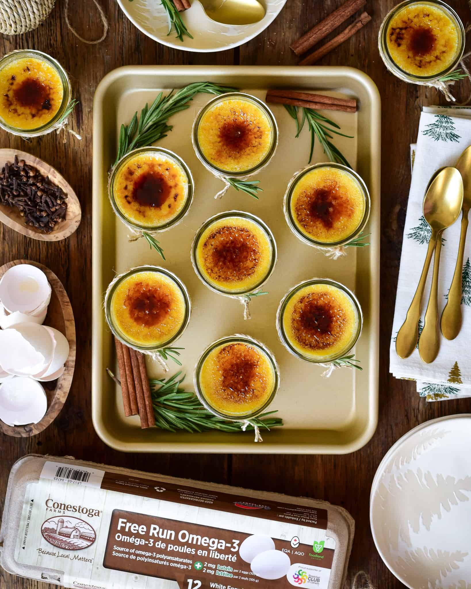 A gold sheet pan with seven festive crème brûlées in mini mason jars.