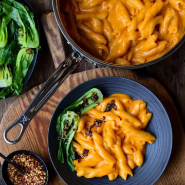 A pot and bowl of creamy Gochujang Mac and Cheese with bok choy and a chili oil drizzle.