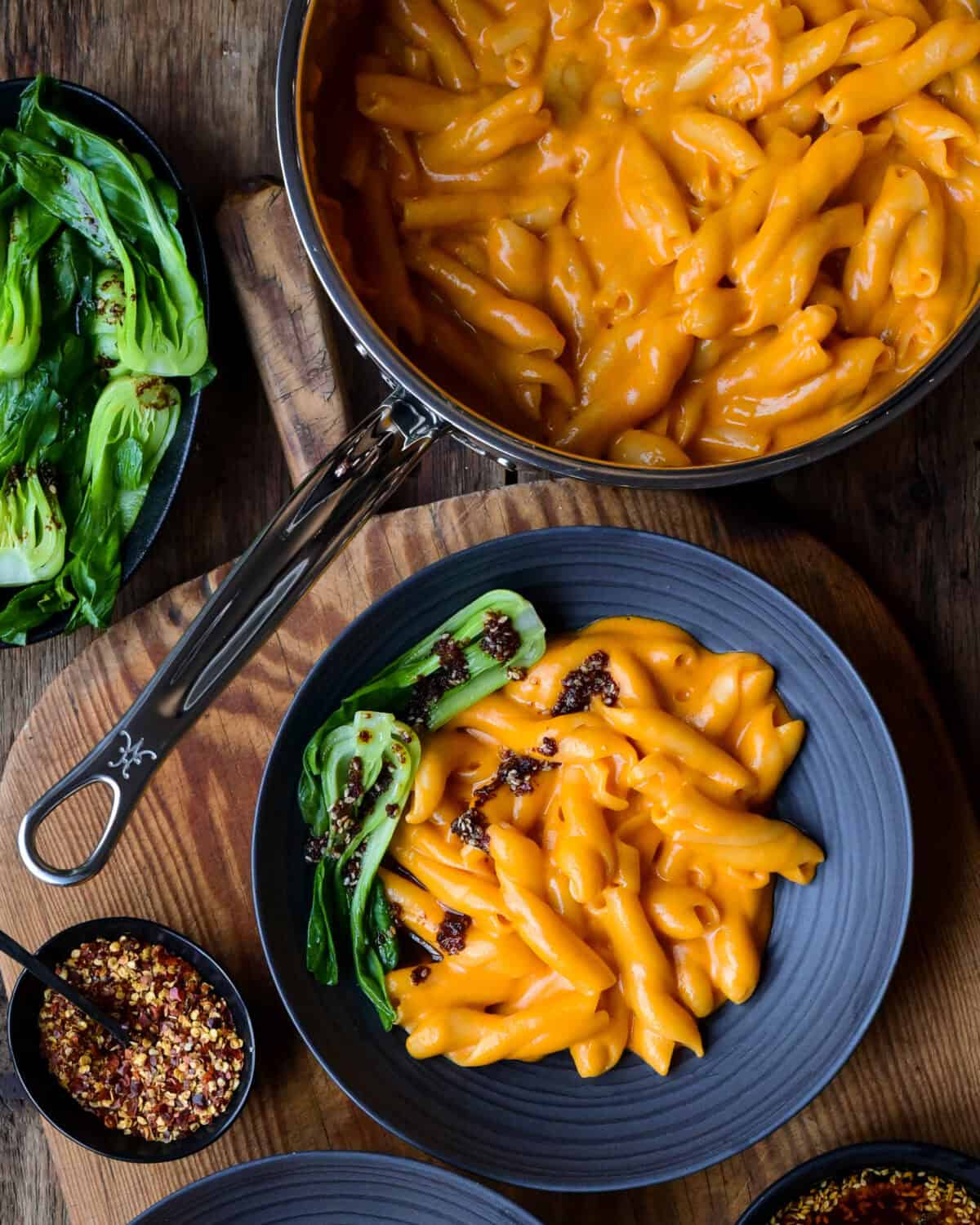 A pot and bowl of creamy Gochujang Mac and Cheese with bok choy and a chili oil drizzle.
