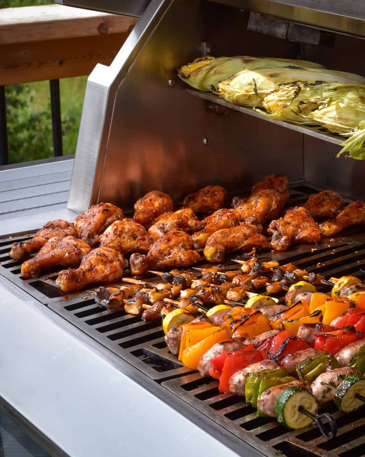 A full grill with gochujang butterflied drumsticks and mini king oyster mushrooms, sausage and pepper skewers and corn on the cob.