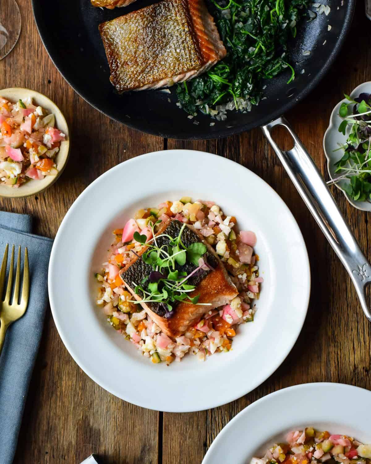 A bowl with Ora King Salmon with Spinach & Chow-Chow beside a pan of Thomas Keller's cookware.