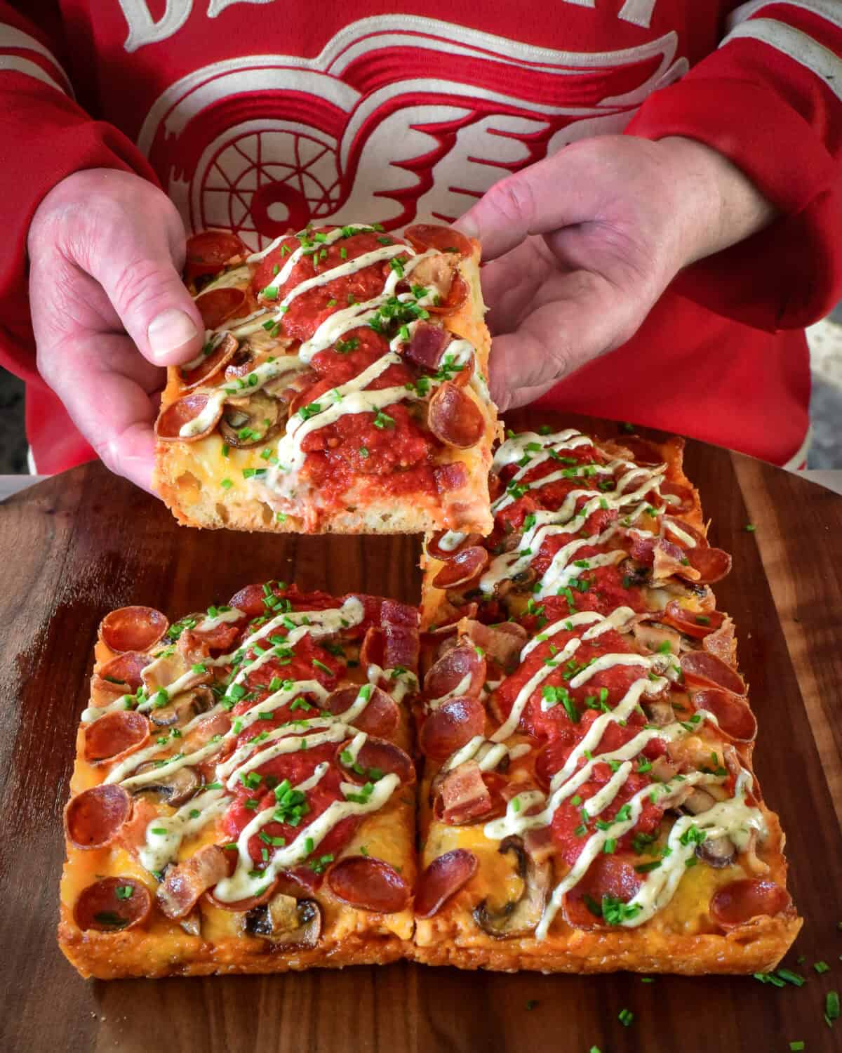 Lifting up a piece of pizza and revealing the iconic Detroit style pizza crust.