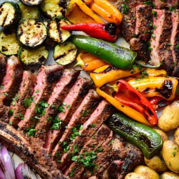 A platter of grilled veggies with sliced steak.
