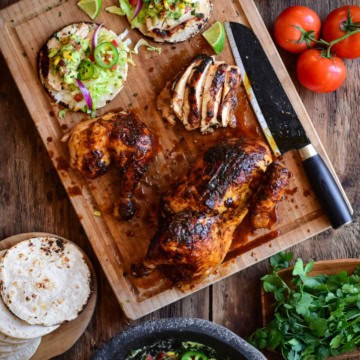 A cutting board with a carved chicken and two tacos. Served with guacamole.