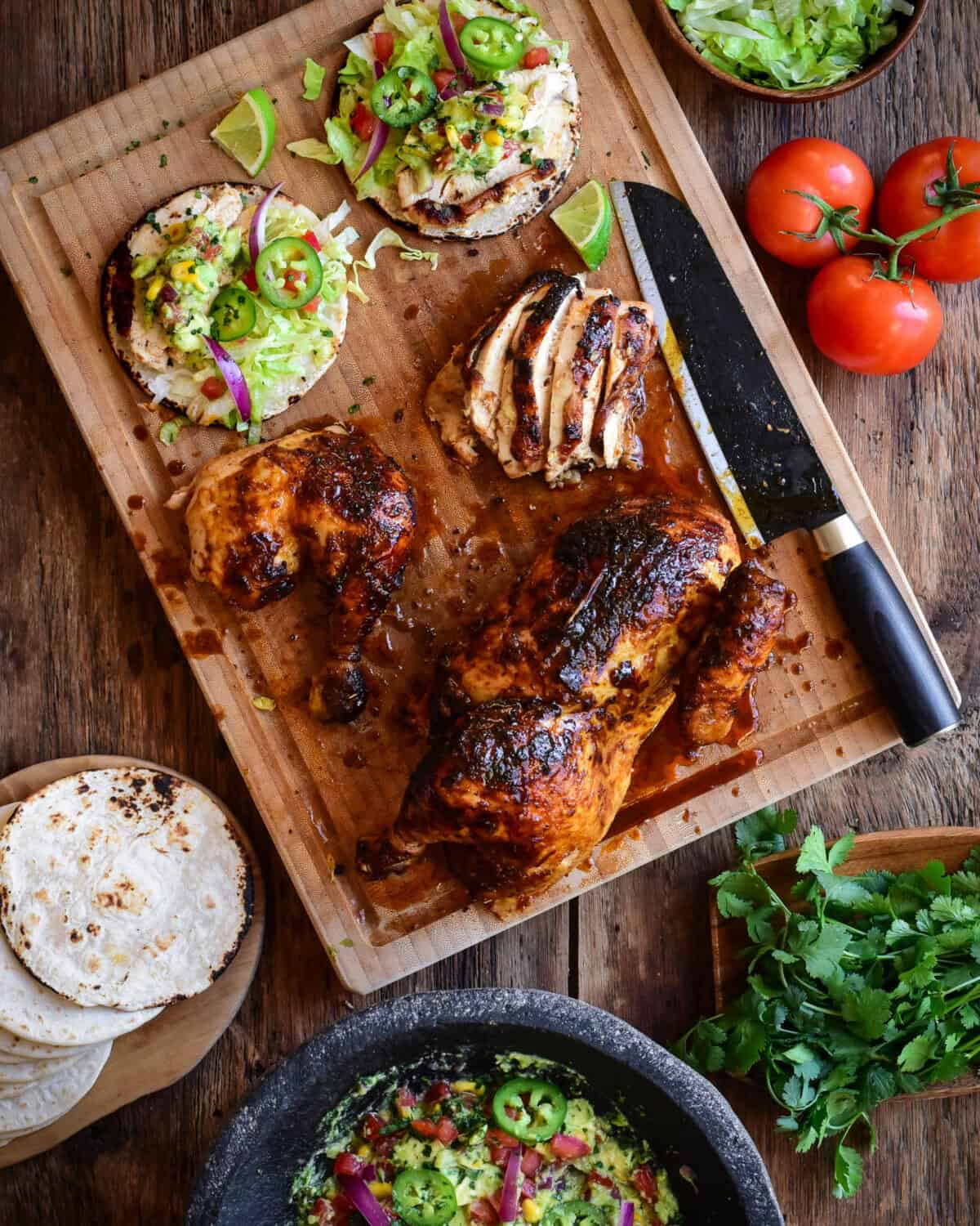 A cutting board with a carved chicken and two tacos. Served with guacamole.