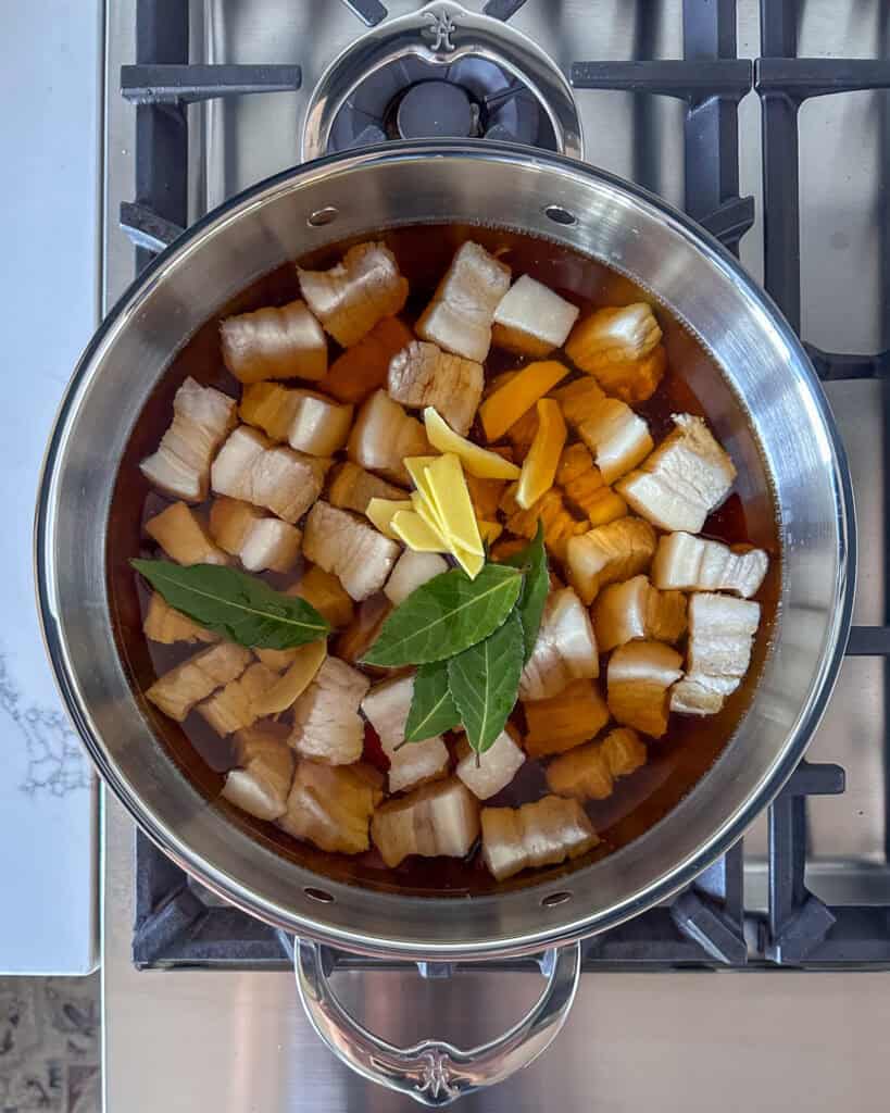 Add the rice wine. Pour enough hot water to just cover the pork belly, then add the light soy sauce, dark soy sauce, ginger, and bay leaves.