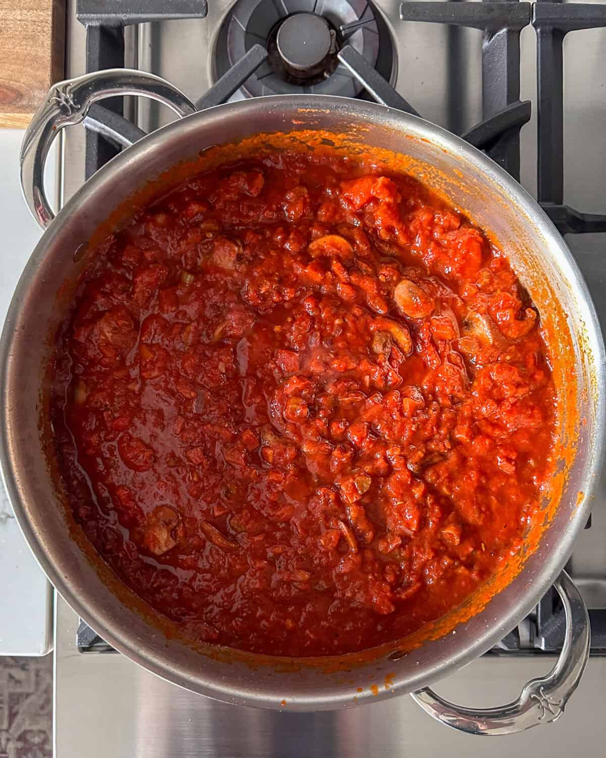 A simmering pot of tomato sauce with bacon, sausage and mushrooms.