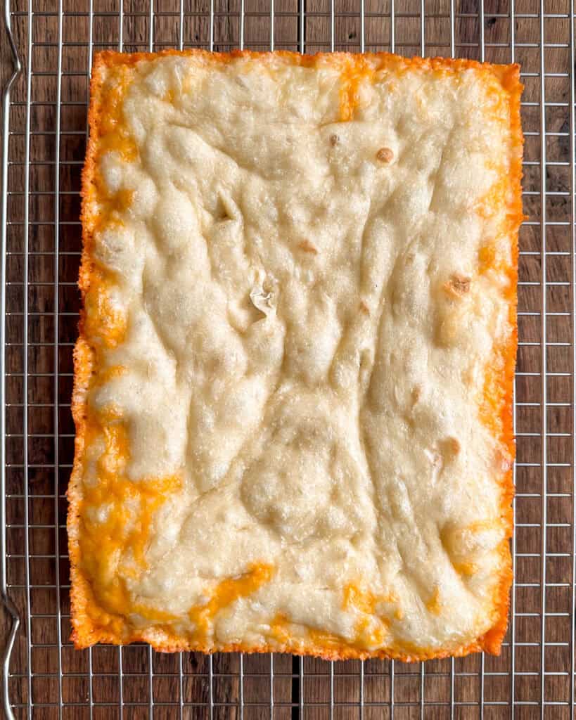 A par-baked Detroit-style pizza dough cooling on a rack.