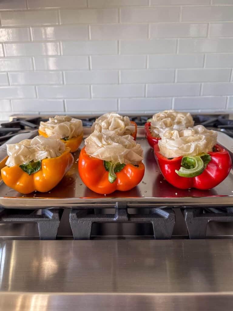 A side view of six tri-coloured stuffed peppers with a scrunched phyllo topping ready to get baked.
