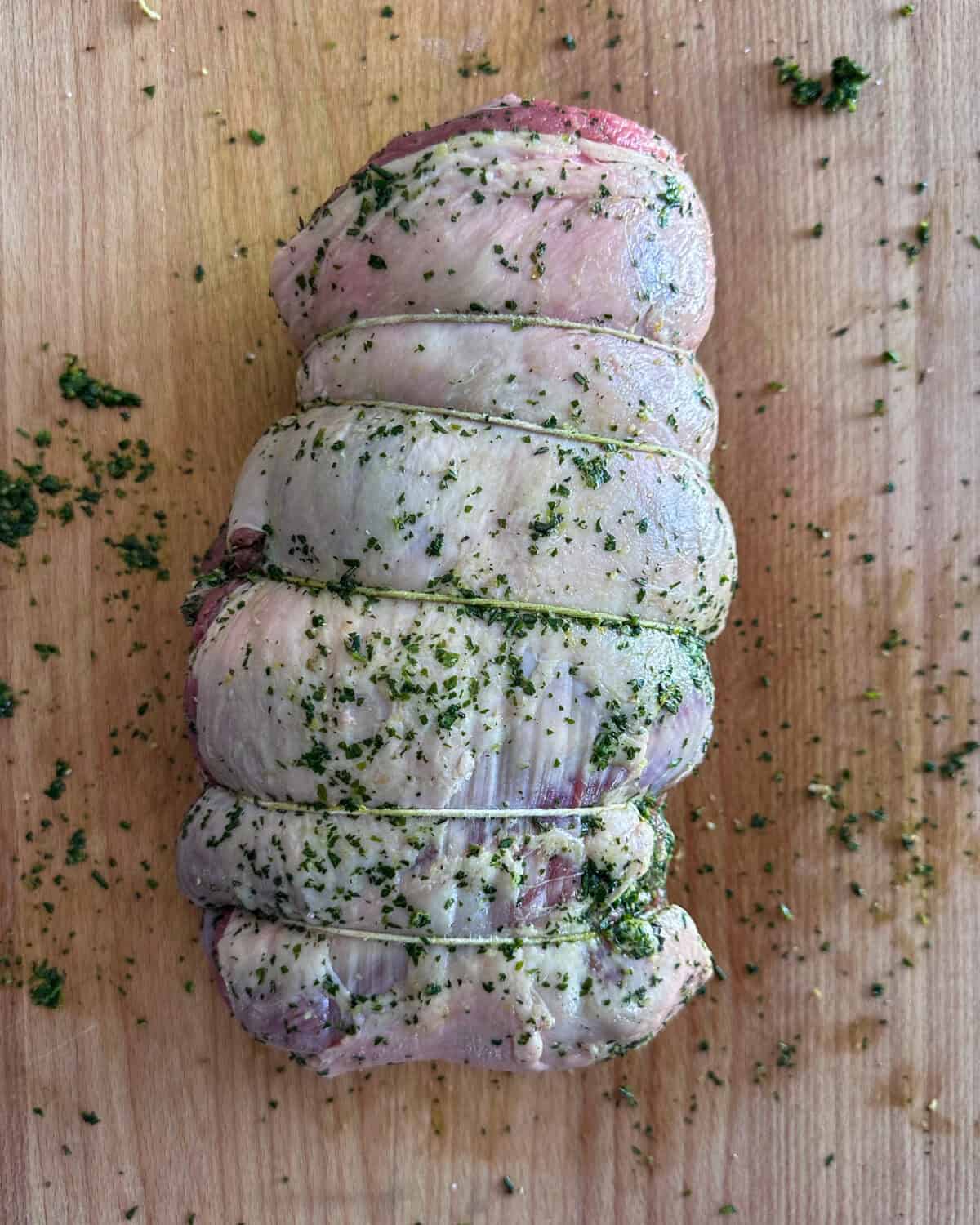 Carefully roll the herb-stuffed boneless Leg of Lamb into a compact cylinder shape, ensuring the herb sauce remains intact inside.