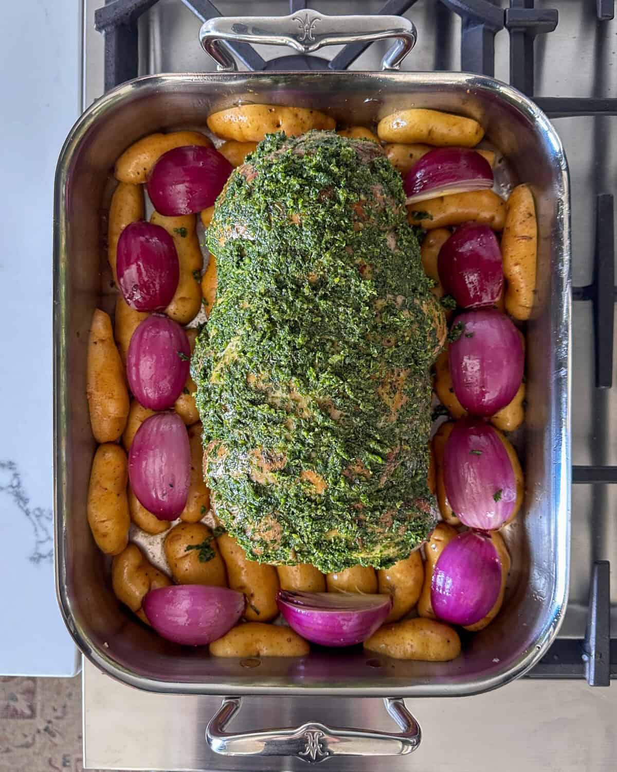 Lay the seared lamb over the potatoes and onions. Rub the outside of the lamb with the remaining herb filling and transfer the roasting pan to a preheated oven.