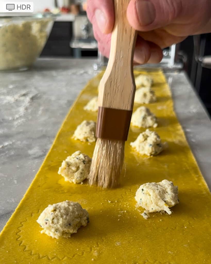 Gently brush water around each mound of filling to help seal the ravioli.